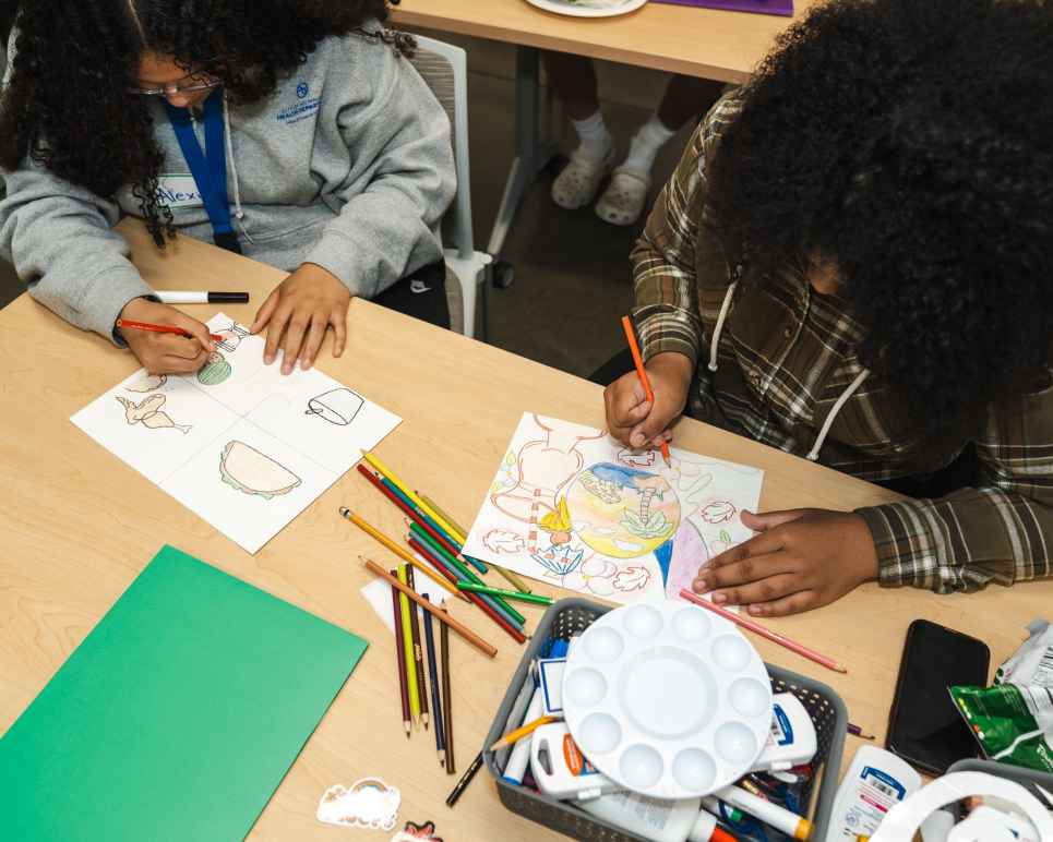 A photo of two studens at a table drawing with art supplies around them